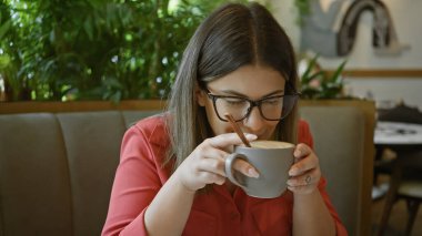 Bardaklı genç bir kadın, doğal bir atmosferi olan rahat bir restoranda otururken kahvenin tadını çıkarıyor..