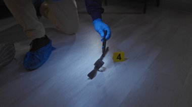 Eldivenli bir adli tıp uzmanı, 4 numaralı sarı işaretle işaretlenmiş kapalı bir suç mahallinde kanıt topluyor..