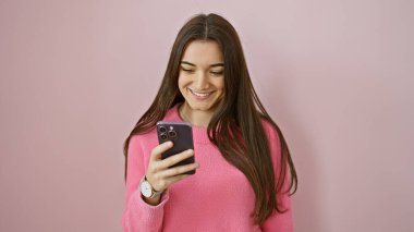 Gülümseyen genç İspanyol kadın pembe izole bir geçmişe karşı akıllı telefon kullanıyor, modern bir gencin yaşam tarzını canlandırıyor..