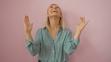 Neşeli bir kadın, orta yaşlı, soyutlanmış, pembe bir duvar arkasındakine karşı deniz mavisi bir gömlek giyiyor, mutlu ve anlamlı, güzel sarışın kadın, genç bir görünüm.