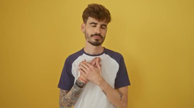 Dövmeleri olan yakışıklı sakallı genç adam, parlak sarı bir arka plana karşı minnettarlık duyuyor.