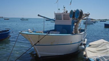 Porto sezaryen limanına demirlemiş geleneksel balıkçı teknesi, parlak bir gökyüzünün altında berrak mavi sularla Puglia ve Salento bölgelerinin cazibesini sergiliyor..