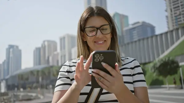 stock image Smiling woman using smartphone in modern dubai cityscape with skyscrapers and urban setting.