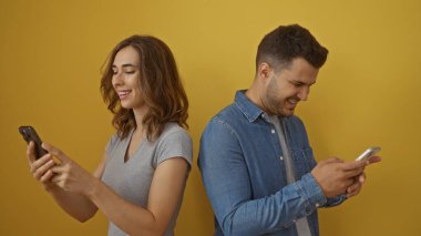 Sarı arka planda akıllı telefonları kullanarak gülümseyen erkek ve kadın bir çiftin ilişkisini ve mutluluğunu basit ve güzel bir ortamda gösteriyor.