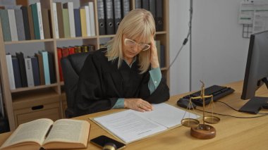 Yargıç ofisinde yasal belgeleri okuyan bir kadın. Masasında adalet terazisi olan bir kadın.