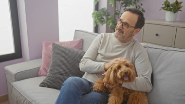 Orta yaşlı İspanyol bir adam evinde evcil kanişiyle rahat bir koltukta rahatlar, memnuniyetini ve dostluğunu ifade eder..