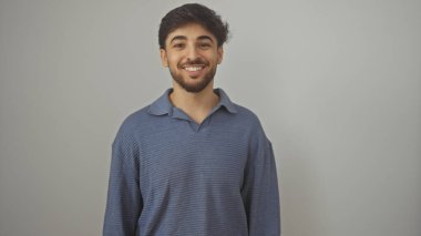 Beyaz bir arka planda günlük kıyafetler giyen sakallı neşeli bir gencin portresi.