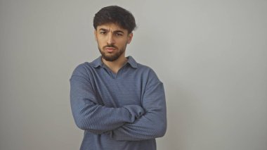 Sakallı genç Arap adam, izole edilmiş beyaz bir arka plana karşı kollarını kavuşturmuş güven içinde poz veriyor..