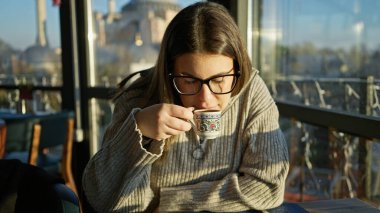 Genç bir kadın İstanbul 'un arka planında Sogia' sı olan bir restoranda kahve içiyor.