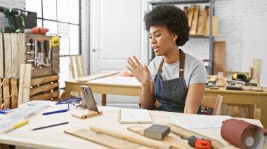 Bir marangoz atölyesindeki Afrikalı Amerikalı kadın bir tablette online bir derse katılıyor.