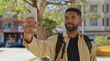 Sakallı Afrikalı genç bir Amerikalı şehir parkı ortamında özçekim yapıyor, rahat ve yakışıklı bir hava yayıyor..