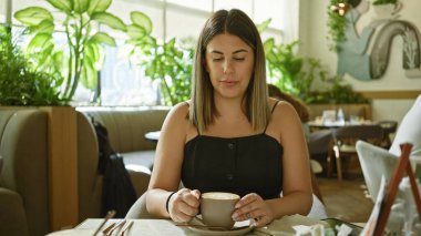 Genç esmer bir kadın, rahat bir kafe ortamında bir fincan kahvenin tadını çıkarıyor..