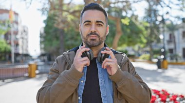 Güneşli bir parkta sakallı, kulaklık takan yakışıklı bir İspanyol..