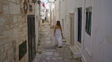 Beyaz elbiseli güzel bir İspanyol kadın Puglia, İtalya ve Avrupa 'daki Ostuni eski kasabasının büyüleyici dar sokaklarında geziniyor..