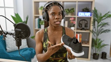 An african american woman with braids talks about sportswear on a radio studio set. clipart