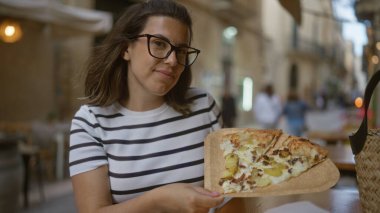 Genç İspanyol kadın İtalyan restoranının terasında lezzetli bir pizzanın tadını çıkarıyor..