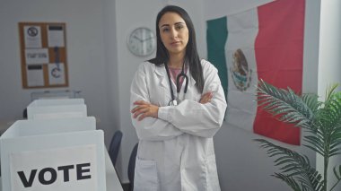 Genç İspanyol bir kadın doktor, Meksika 'da bir oy odasında güven içinde duruyor. Kabinleri ve bayrakları var..