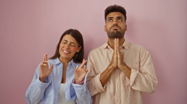 Man and woman crossing fingers and praying together against pink background, expressing hope and anticipation. clipart