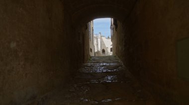 Materya, bazilika ve İtalya 'da dar, parke taştan bir ara sokak. Açık mavi gökyüzünün altındaki tarihi taş binaların parlak manzarasını gösteriyor..
