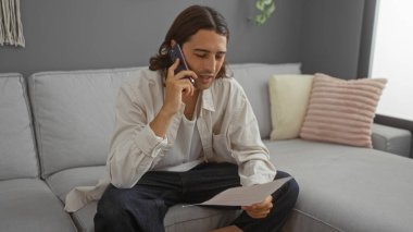 Sıcak bir oturma odasında dokümanları okurken telefonda konuşan İspanyol genç adam.