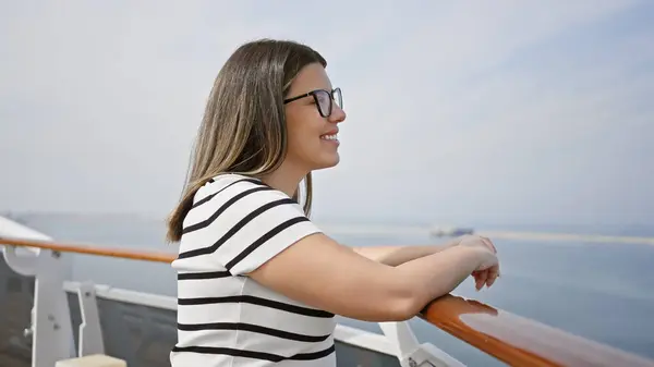 stock image Smiling young woman leaning on a cruise ship railing overlooking the ocean under a clear blue sky.