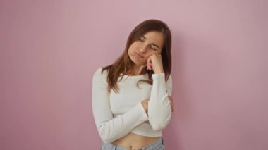 Genç bir kadın, yorgun, sarışın bir figür çapraz kollarla ayakta duruyor ve düşünüyor, depresyon ve sıkıntıyla mücadele ediyor - pembe bir arka planda izole edilmiş.