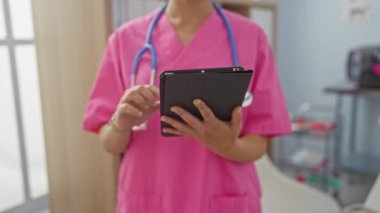 Hastane odasında steteskoplu pembe önlüklü kadın doktor tablet kullanıyor..