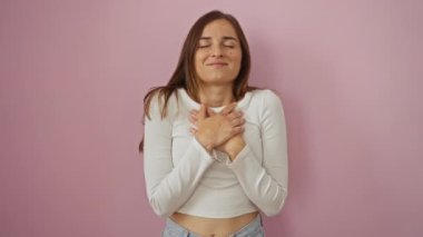Minnettar bir jestle ellerini göğsüne koyup duran genç sarışın kadın, sağlık ve refah için izole edilmiş pembe arka planda kapalı gözlerle gülümsüyor.