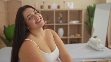 Güzellik salonunda arka planda bitki ve raflarla gülümseyen bir kadın.