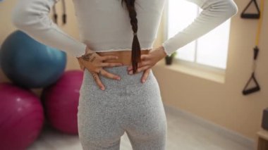 Beden eğitiminde elleri ağrılı genç bir kadın, arka planda egzersiz topları, iç dekorasyon.