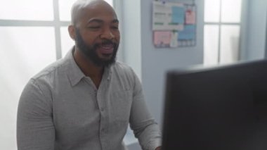 Ofis ortamında çalışan genç bir adam, içeride bilgisayar ekranının önünde gülümseyen sakallı, kel ve yakışıklı bir zenci..