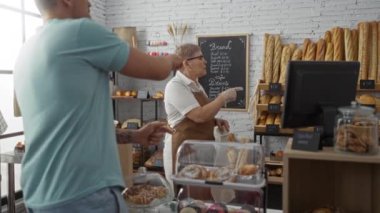 Kadın ve erkek birlikte bir fırında çalışıyor çeşitli ekmek ve hamur işleri sergileniyor, içerideki rafları düzenlerken sohbet ediyorlar..