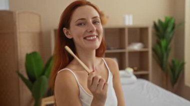 Kaplıcada elinde diş fırçası olan gülümseyen bir kadın. Arka planda bitki ve raflar var.