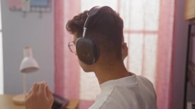 Ofis ortamında kulaklık takan genç İspanyol bir adam. Masasında lamba ve telefonla oturuyor..