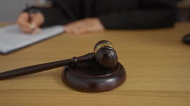 Yargıç, adalet, hukuk, düzen ve karar verme sürecini temsil eden tahta bir masa üzerinde tokmak ile mahkeme salonunda yazı yazıyor.