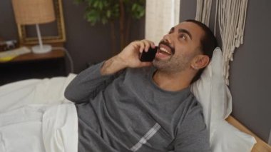 Sıcak bir yatak odasında yatakta uzanmış telefonda konuşan yakışıklı bir adam.