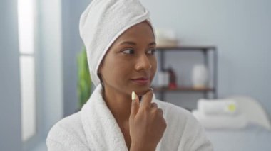 Young woman with a towel on her head and a white robe, enjoying a spa treatment in a relaxing beauty center with modern wellness facilities