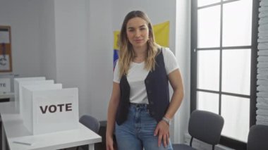 Venezuela 'da bir seçim koleji odasında kollarını kavuşturmuş, oy verme kabinlerinin ve Venezuela bayrağının önünde genç, çekici, beyaz bir kadın duruyor..
