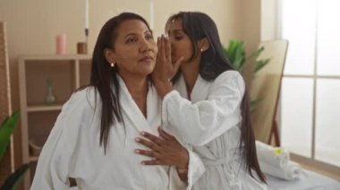 Spa elbiseli anne ve kız bir sağlık merkezinde fısıldaşıp kaynaşıyorlar, yakın ilişkilerini ve rahatlıklarını kapalı bir ortamda sergiliyorlar..