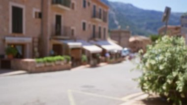 Güneşli bir günde Bokeh, mağaza önleri ve bitkilere odaklanarak Mallorca, İspanya 'daki bir sokak sahnesinin bulanık arkaplanı rahatlatıcı bir ortam yaratıyor.
