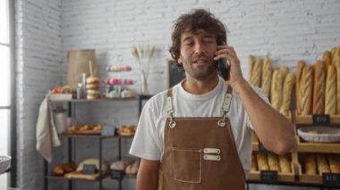 Genç adam fırının içinde telefonla konuşuyor. Arkaplanda da raflar dolusu ekmek var.