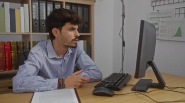 Ofis ortamında sakallı, çizgili gömlek giyen, bilgisayar ekranında el ele tutuşan, belgelerle ve kitaplıklarla çevrili genç bir adam, iş sıkıntısı olduğunu gösteriyor.