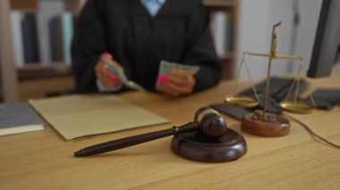 Kadın yargıç büro masasında ön planda tokmak ve teraziyle para sayıyor. Hukuk ve adaleti simgeliyor.