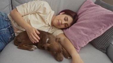Genç bir kadın, rahat oturma odasında köpeğiyle kanepede uyuyor..