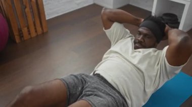 Çağdaş bir spor salonunda mavi bir paspasın üzerinde egzersiz yapan Afrikalı Amerikalı bir adam..