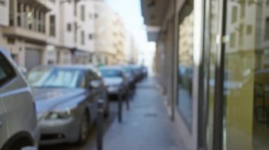 Güneşli bir günde şehir dışında bulanık arabaların ve binaların olduğu bir sokak manzarası.