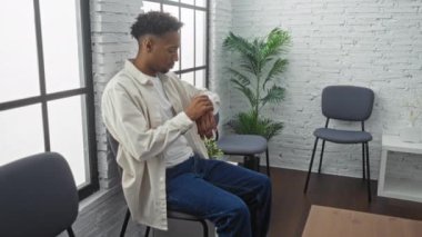 Yakışıklı, sakallı, bekleme odasında oturan, saatini kontrol eden, modern bir iç mekan ve şık mobilyalar sergileyen Afro-Amerikan bir adam..