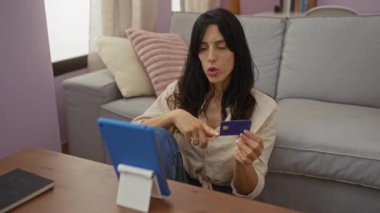 Oturma odasında video görüşmesi yapan bir kadının elinde kredi kartı var.