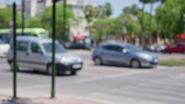 Güneşli bir günde arka planda bulanık arabaların, ağaçların ve binaların olduğu odaksız sokak sahnesi