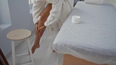 Sağlık merkezindeki bacaklar için spa 'ya losyon süren bir kadın. Yanında da kaplıca ve ahşap bir tabure var.